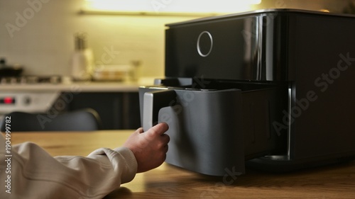 Close-up of a person's hand pulling out the drawer of a modern black air fryer