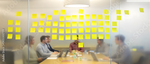 Collaborative business team brainstorming behind a glass wall filled with yellow sticky notes, focusing on agile project management strategy and creative ideas in a modern corporate conference room.