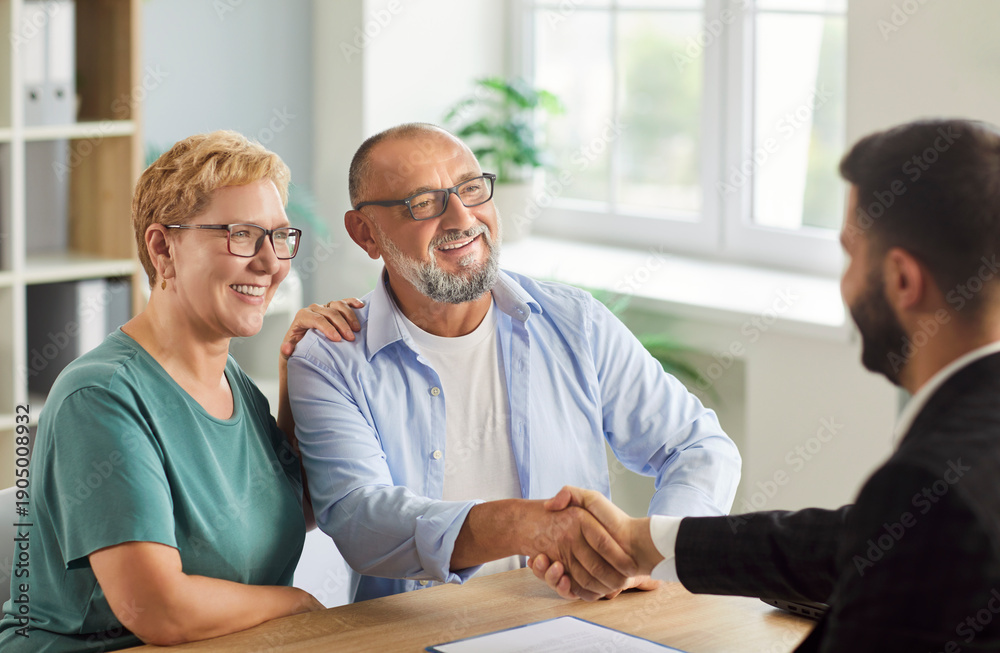Fototapeta premium A senior couple meets their advisor in office, shaking hands to finalize a retirement agreement and financial planning. Smiling man and woman make a deal about insurance with male agent. 