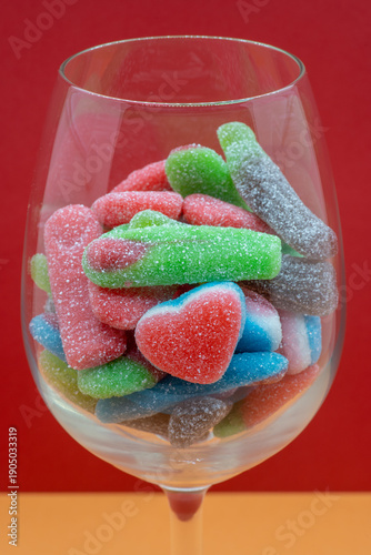 Assorted sugar-coated gummy candies filling a wine glass on a red background