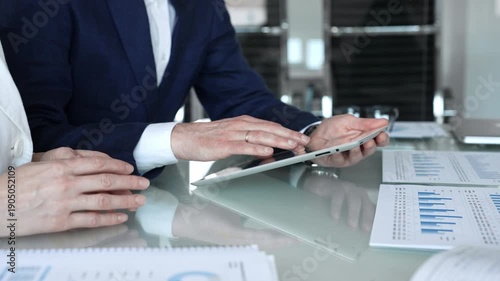 Business partners collaborating on a digital tablet, analyzing financial data and reports during a corporate meeting in a modern office, planning strategies for growth