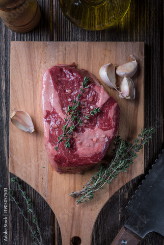 Raw ribeye steak with garlic and thyme on a wooden board, top view.