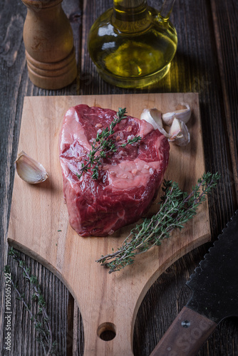 Raw ribeye steak with garlic and thyme on a wooden board, top view.