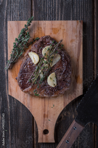 Grilled ribeye steak with garlic and thyme on a wooden table, top view.