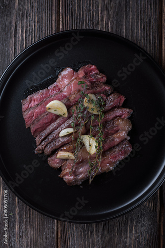 Grilled rib eye steak cut on black plate on wooden table, top view.