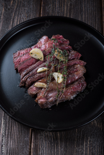 Grilled rib eye steak cut on black plate on wooden table, top view.