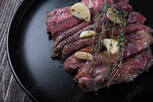 Grilled rib eye steak cut on black plate on wooden table, top view.