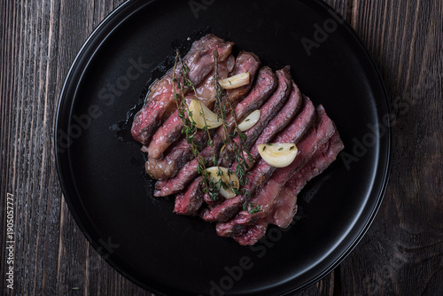 Grilled rib eye steak cut on black plate on wooden table, top view.