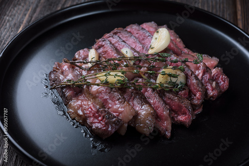 Grilled rib eye steak cut on black plate on wooden table, top view.