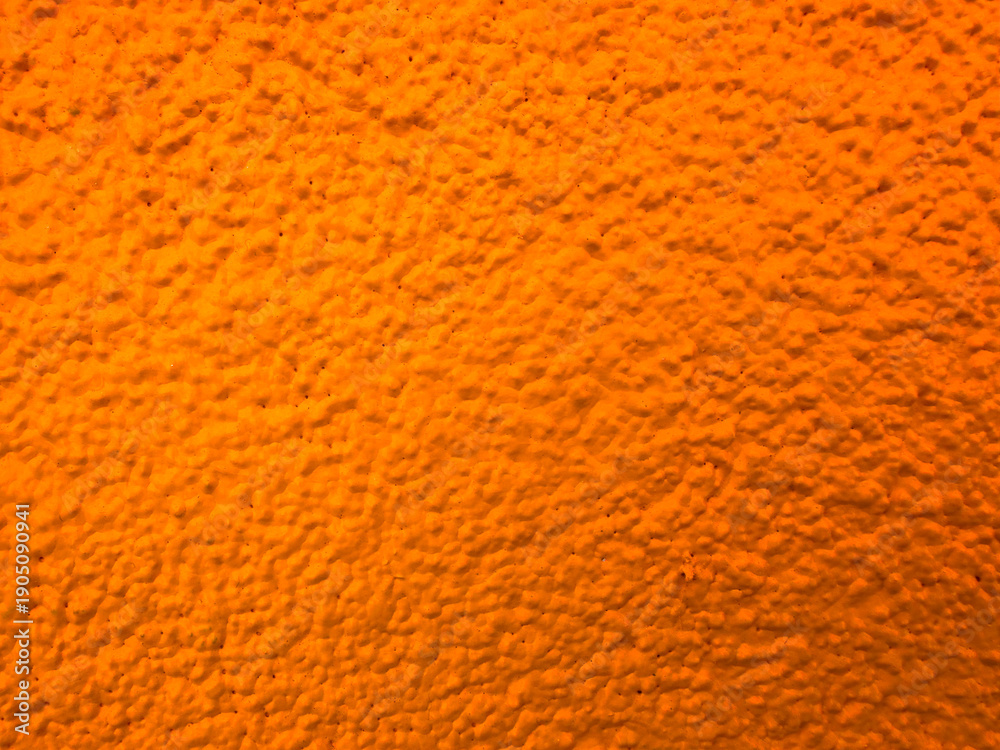 Naklejka premium Close-up view of an orange painted stucco wall featuring a rough textured surface, ideal for vibrant backgrounds, design accents, and abstract compositions.