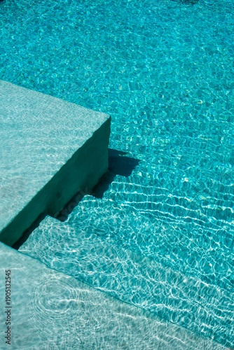 Fotografi Vista detallada de una piscina con agua turquesa cristalina y reflejos de luz natural sobre superficie arquitectónica moderna