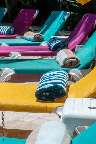 Filas de camastros coloridos con toallas enrolladas junto a una piscina en resort tropical. Escena vibrante que representa vacaciones, descanso, verano y turismo en destino soleado.