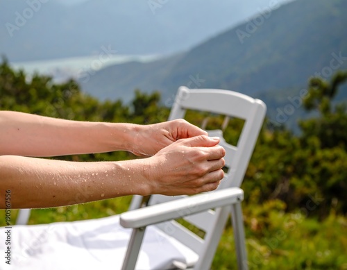 Close-up of human hands with water droplets, in front of a white chair and scenic mountain range