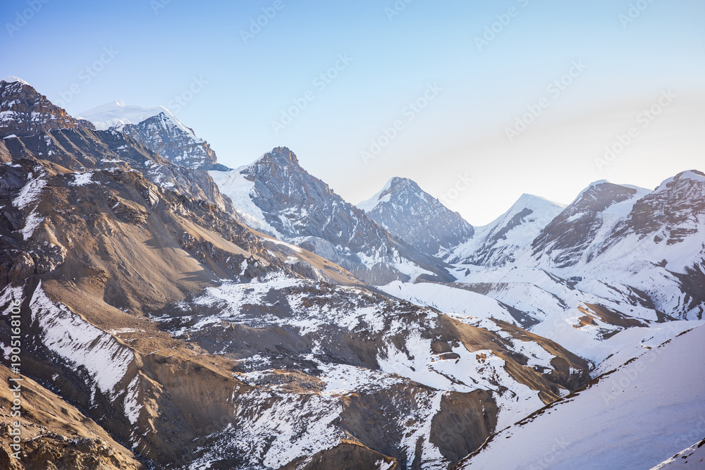 Fototapeta premium Expansive view of a dramatic Himalayan mountain valley with rugged peaks, snow-covered slopes, and exposed rocky terrain under a clear blue sky. The vast scale and raw alpine landscape evoke freedom