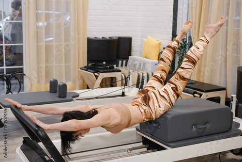 Mature woman in her 40s performing advanced reformer pilates in standing balance exercise for core strength and flexibility. Female improving balance through low-impact mindful movement