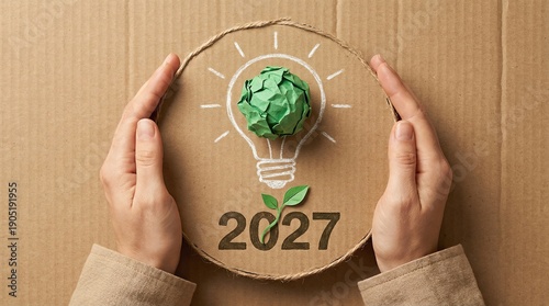 Sustainable idea for 2027 – hands protecting eco light bulb symbol on cardboard background