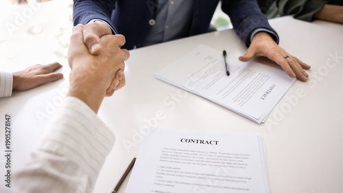 Cuadro en lienzo Close up image of two men firmly shaking hands over desk, symbolizing successful closing of business deal, seated at table with signed contract papers