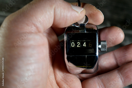 hand with a mechanical hand tally counter, a handheld, battery-free device used for manual counting, used for tracking laps, inventory, Tasbih counting in Islam, guest counts, and traffic