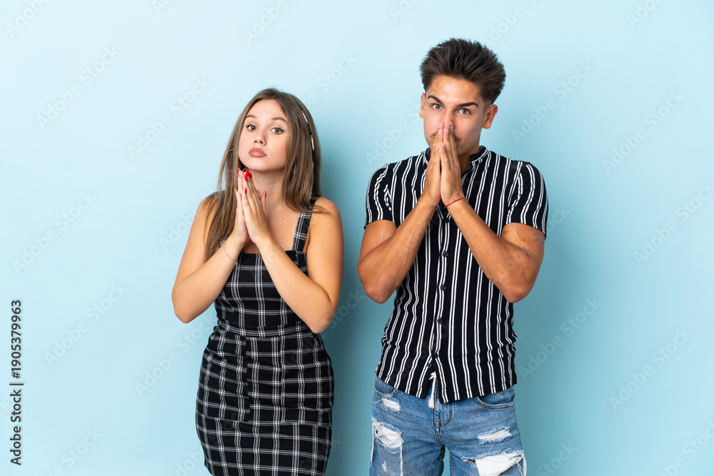 Naklejka premium Teenager caucasian couple isolated on blue background keeps palm together. Person asks for something