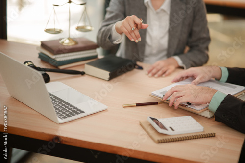 lawyer and a client discussing documents in a law firm. The desk features legal symbols like a lady justice scale, a gavel, law books, a laptop, and a calculator, representing a blend of legal and fin