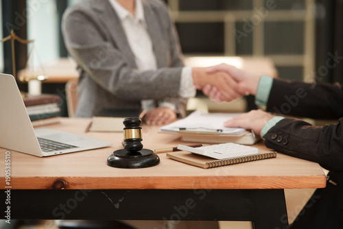 lawyer and a client discussing documents in a law firm. The desk features legal symbols like a lady justice scale, a gavel, law books, a laptop
