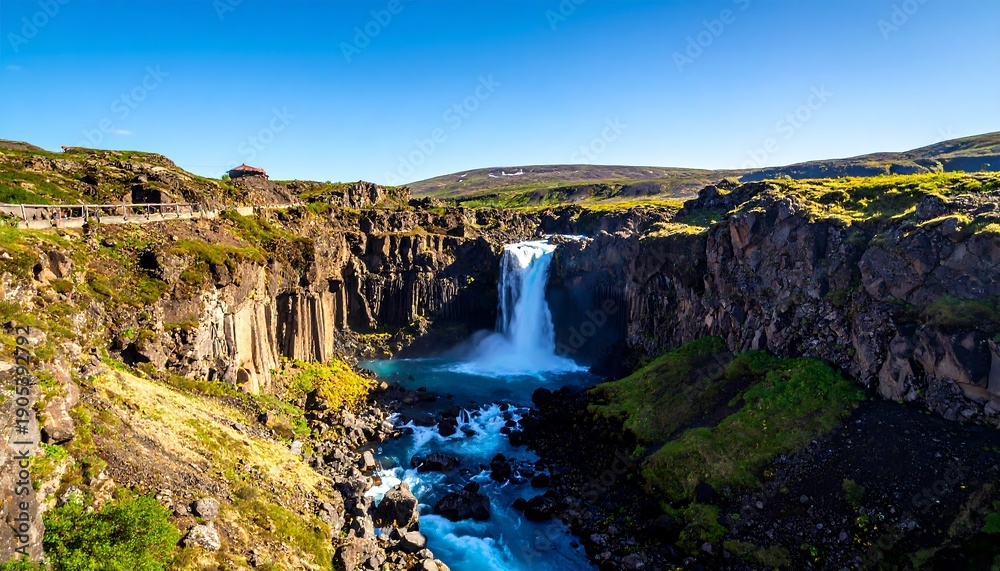 Obraz premium A stunning view of a powerful waterfall cascading into a deep canyon under a clear blue sky. Rugged cliffs frame the scene