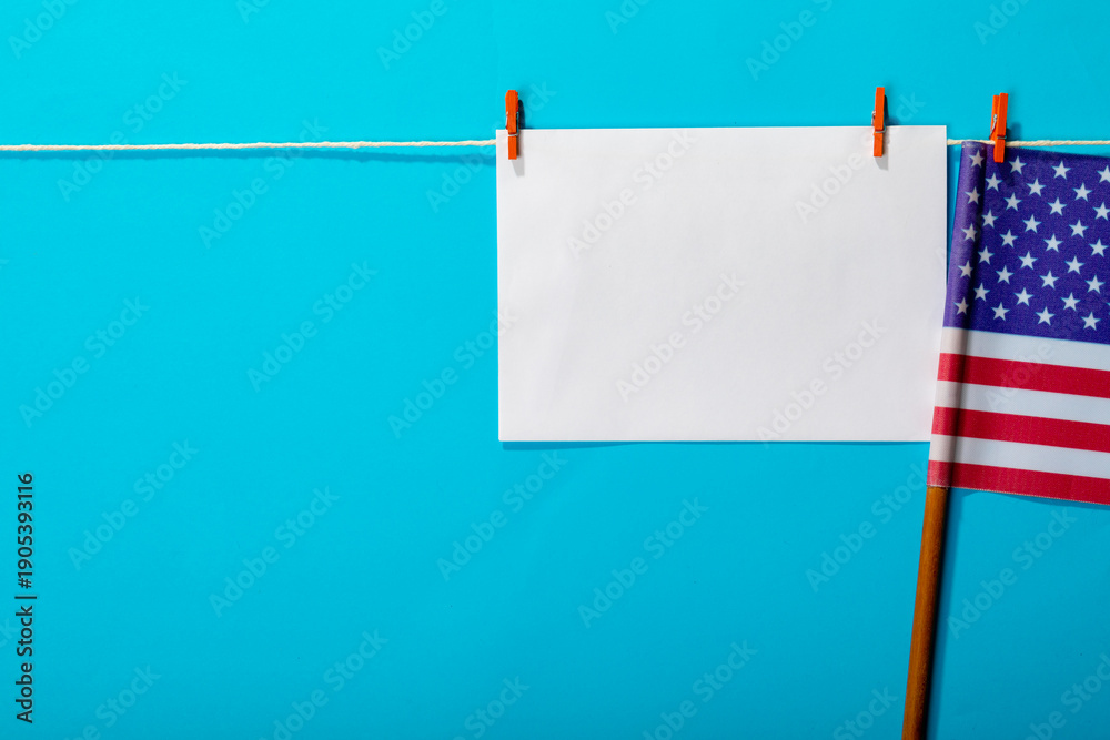 Obraz premium Blank paper with copy space hanging by america flag hanging from clothesline on blue background