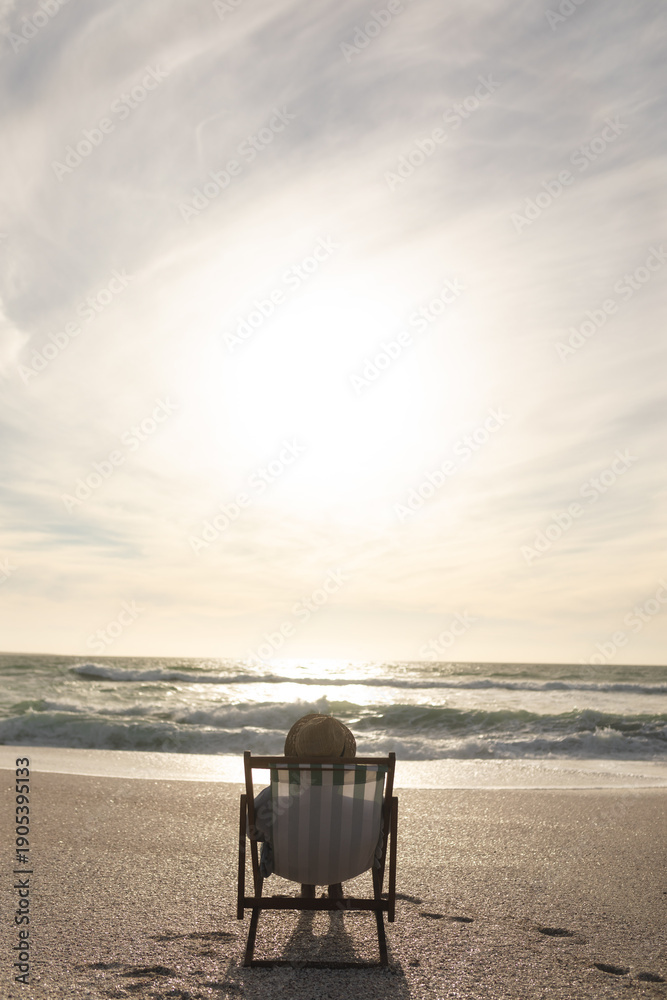 Obraz premium Senior woman sitting on folding chair relaxing at beach in front of horizon over sea