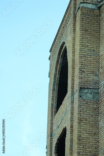 A close-up view of a brick building facade with arched windows against a blue sky.
