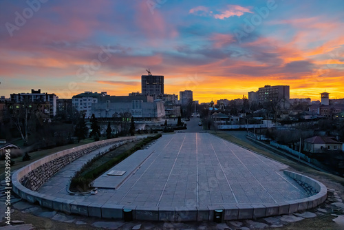 Cherkasy urban view at twilight, showing city architecture and a large paved public square, with vibrant orange and blue clouds painting the sky during a colorful sunset