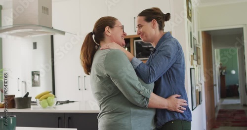 Caucasian lesbian couple smiling and dancing in kitchen