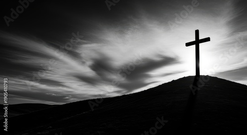 Dramatic black and white silhouette of the crucifixion cross stands on a hill under a somber, cloudy good friday sky.