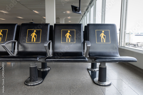 Row of airport seats marked with yellow elderly icons in a bright terminal waiting area. Priority seating reserved for seniors and passengers needing assistance. Travel and accessibility theme
