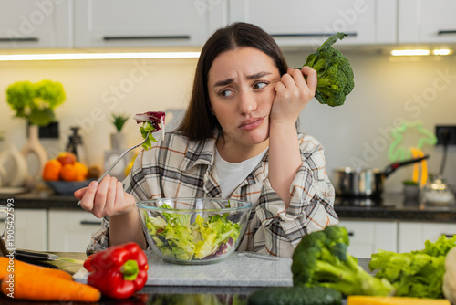 Foto Young woman eats vegetable salad and looks drained after strict keto diet, craving comfort food