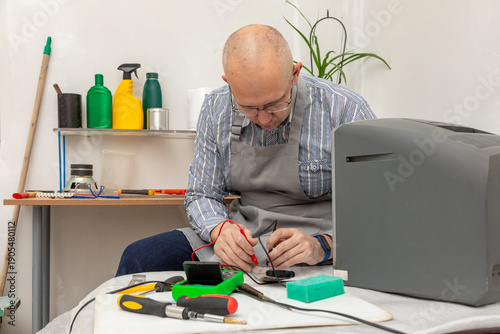 Fotografie A man with glasses and apron using a multimeter to repair an old television