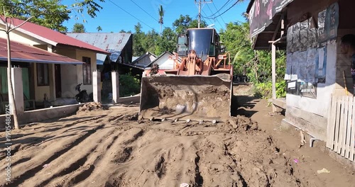 Bulldozer leveling muddy ground between residential buildings.