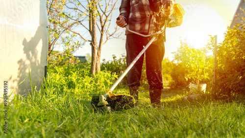 Foto A gardener with a lawn trimmer mows the grass on the property