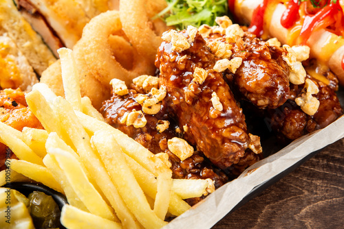 Fotografie A high-angle close-up of a delicious assorted fried food platter featuring saucy chicken wings, crispy french fries, and golden onion rings, served on paper for a casual meal or appetizer