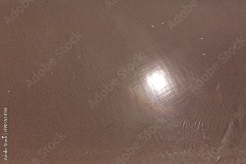 Close-up view of water flowing over wet sand, creating dynamic, natural patterns, featuring ripples and reflections of sunlight on the shallow water, Saaremaa, Estonia, Europe.