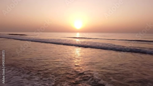 Tranquil beach scene at sunrise with calm waves and the sun's reflection