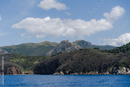 Rocky coastline with green hills and calm sea under blue sky.