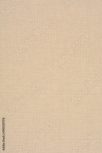 A full frame shot of a beige waffle weave fabric displaying a uniform square grid pattern with natural cotton fiber details