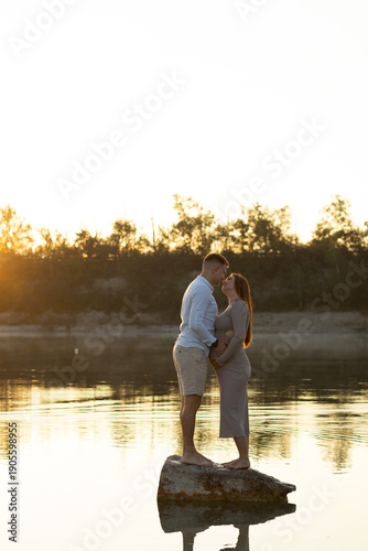 A man and a woman enjoying a moment by the water at sunset. Calm nature, reflection in the lake and soft golden light create an atmosphere of privacy and harmony.