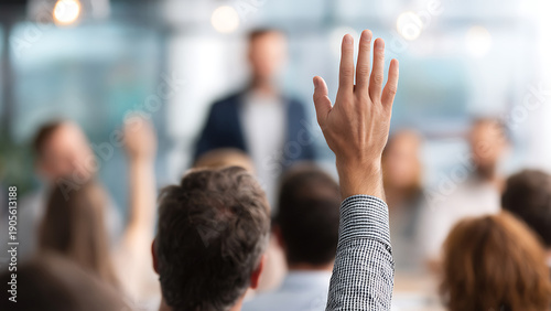Vibrant Close-up of a Hand Raised for Question Amidst a Blurred Conference Audience