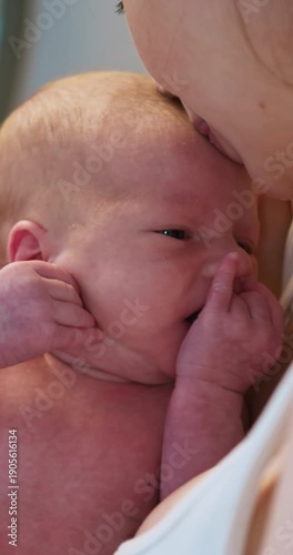 Close-up of tiny newborn baby with eyes closed, finger touching mouth, held by parent