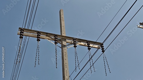 Broken high voltage electrical power line jumper wire hanging from concrete pole causing blackout and danger risk against grey sky.
