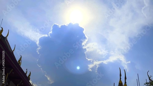 The Sun's Shining Behind Big Cloud and Parts of Roofs of Temple on Blue Sky Background with Bird Flying Compound of a Monastery at Bangkok, Thailand. 19 MAY 2025, A.M./ Real Time Video
