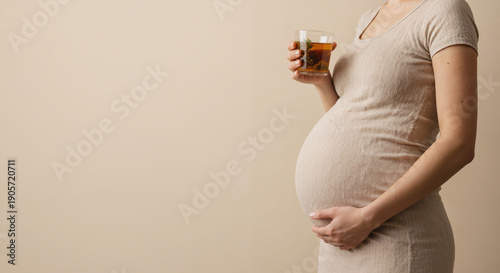 Pregnant woman holding a glass of beverage while touching her belly in a serene moment copy space