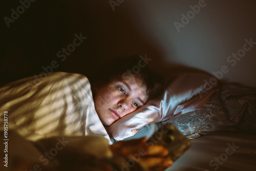 young woman uses smartphone at night while lying in bed