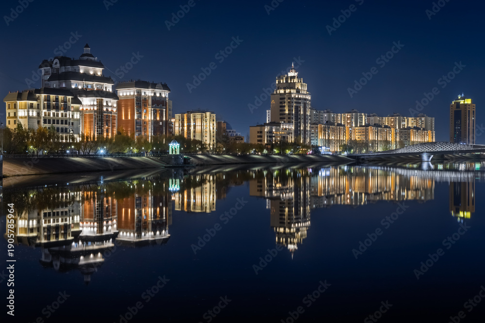 Fototapeta premium Modern buildings, the embankment and the bridge are reflected in the water of the Ishim (Esil) river in Astana, the capital of Kazakhstan